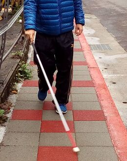 Photo of a person from the waist down, walking with a white cane.